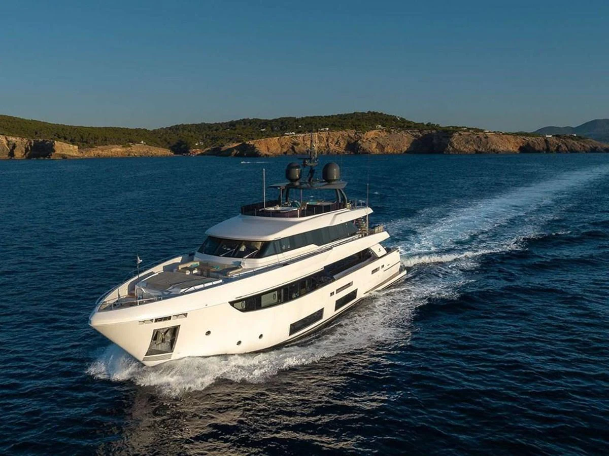A sleek, modern yacht cruises through clear blue waters with a scenic coastline in the background. aboard ON Yacht for Sale