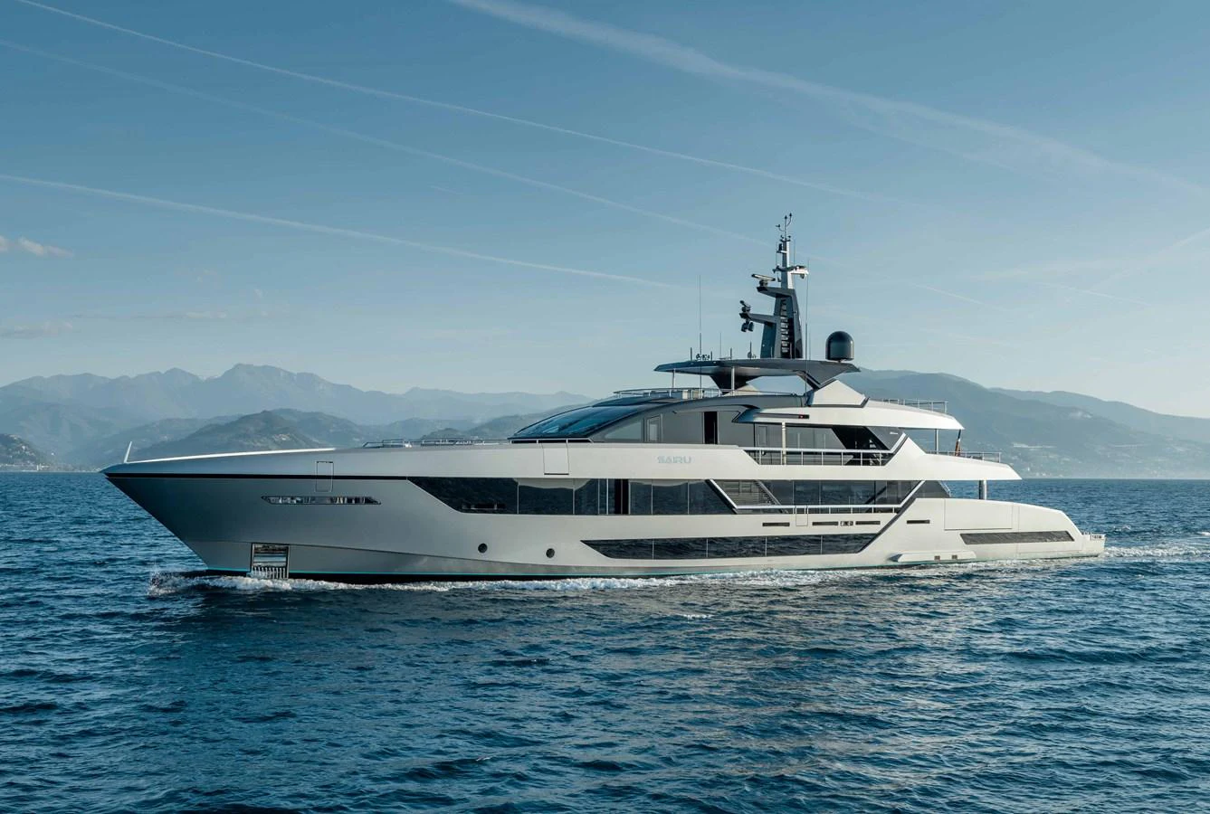 A sleek and modern yacht cruising on calm waters with a mountainous backdrop. aboard SAIRU Yacht for Sale