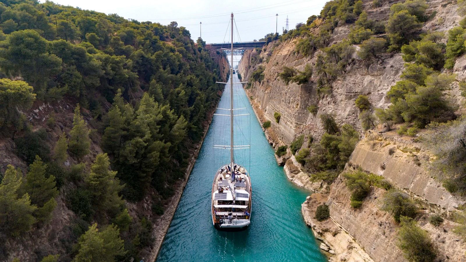 A yacht navigates through a narrow canal surrounded by lush greenery and rocky cliffs. aboard ODISEA Yacht for Sale