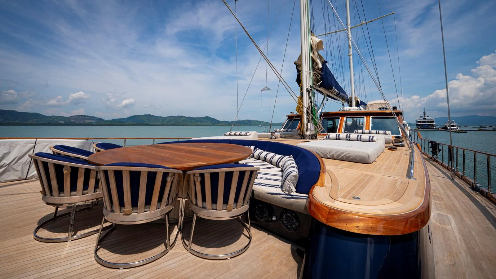 The yacht's deck features a spacious seating area with a large wooden table and comfortable striped cushions, perfect for outdoor relaxation and dining. aboard ODISEA Yacht for Sale