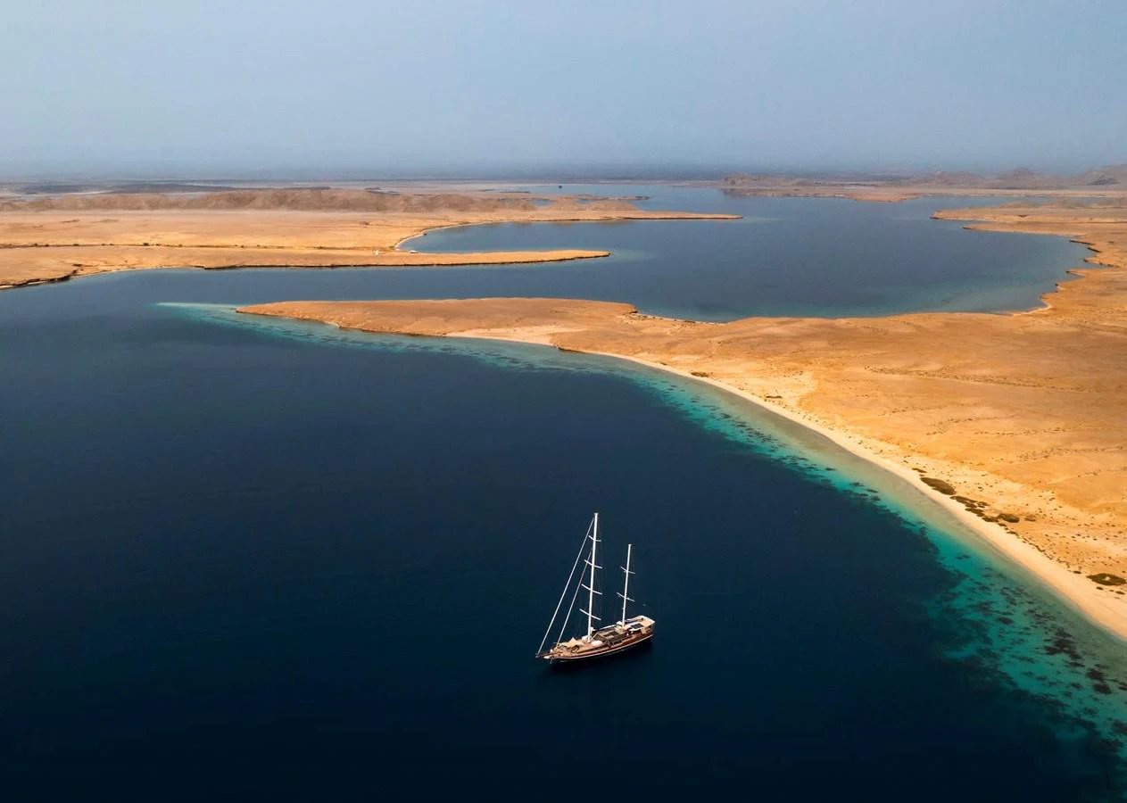 A stunning yacht sails gracefully along a serene coastline with pristine waters and golden sands. aboard ODISEA Yacht for Sale