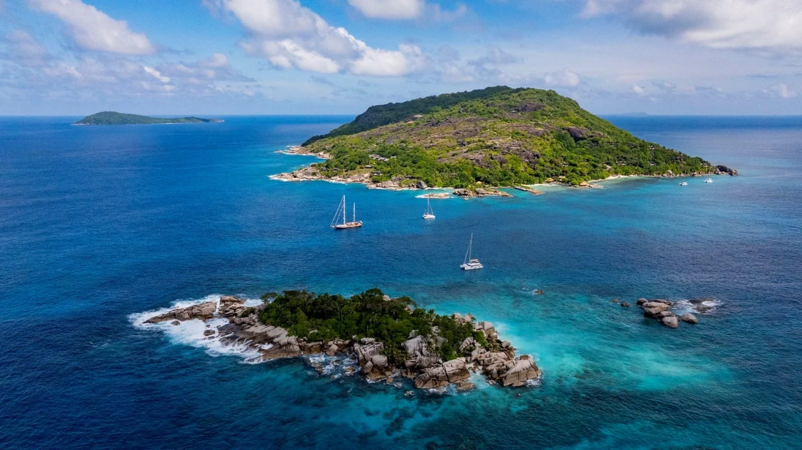 A serene view of yachts anchored near a lush, tropical island with clear blue waters. aboard ODISEA Yacht for Sale