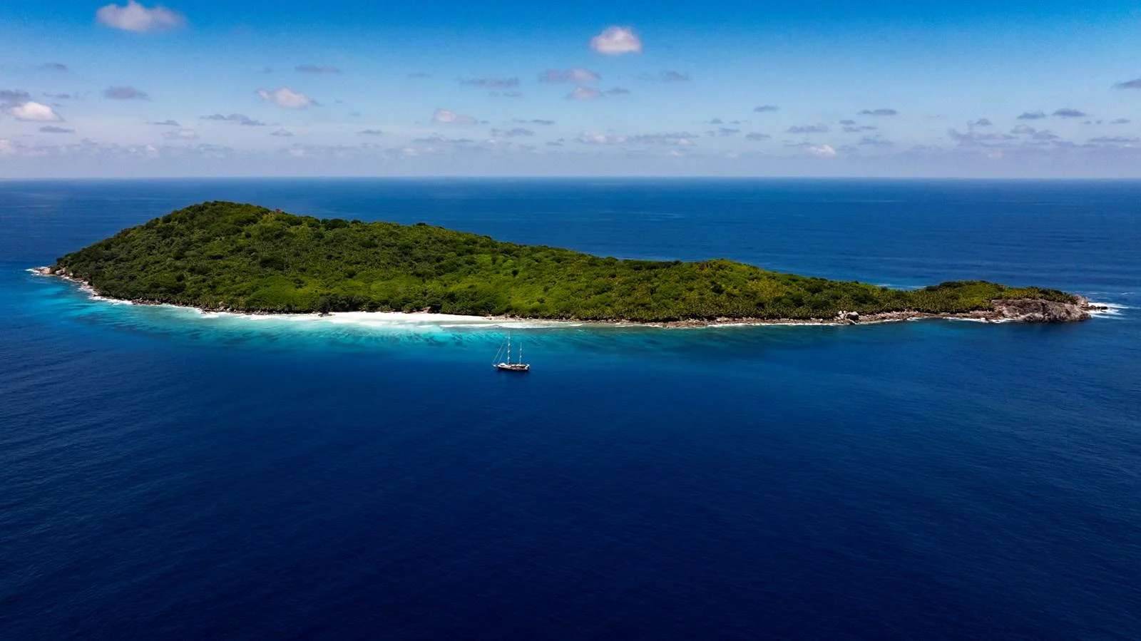 A yacht is anchored near a lush, secluded island surrounded by clear blue waters. aboard ODISEA Yacht for Sale