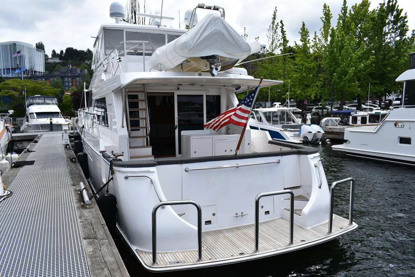 The yacht is docked, showcasing its spacious aft deck with an American flag and a tender stored above. aboard 64 OCEAN ALEXANDER Yacht for Sale