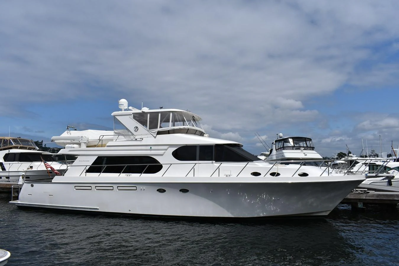 A sleek white yacht is docked at a marina under a partly cloudy sky. aboard 64 OCEAN ALEXANDER Yacht for Sale