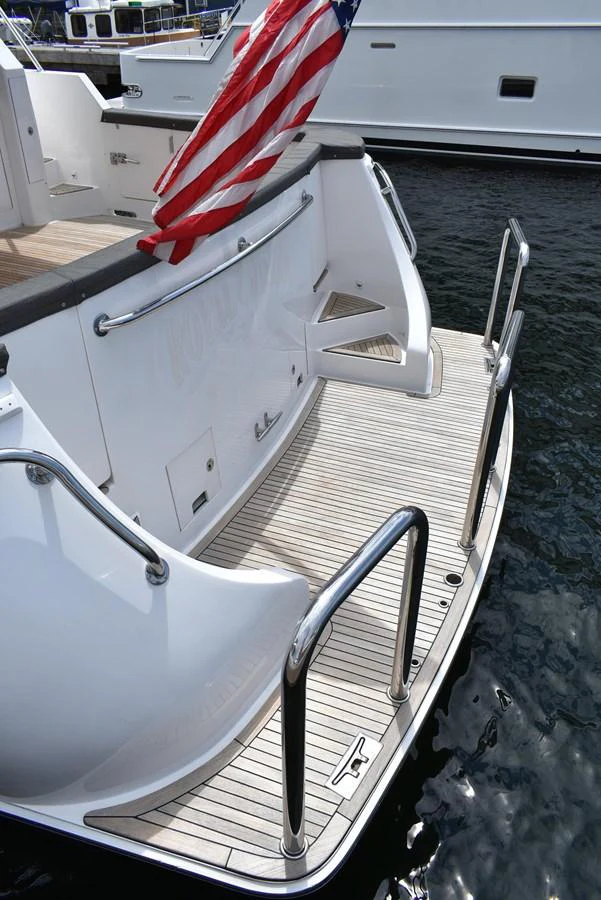 The yacht's swim platform features a sleek design with polished metal railings and a flag. aboard 64 OCEAN ALEXANDER Yacht for Sale