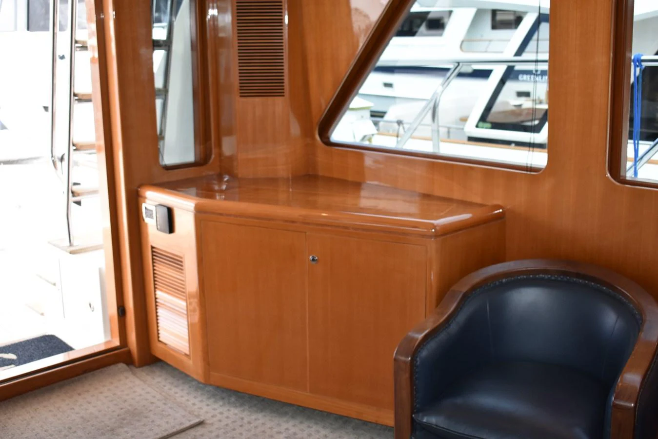 The yacht's interior features a polished wooden cabinet and a comfortable leather chair, with large windows providing a view of the marina. aboard 64 OCEAN ALEXANDER Yacht for Sale