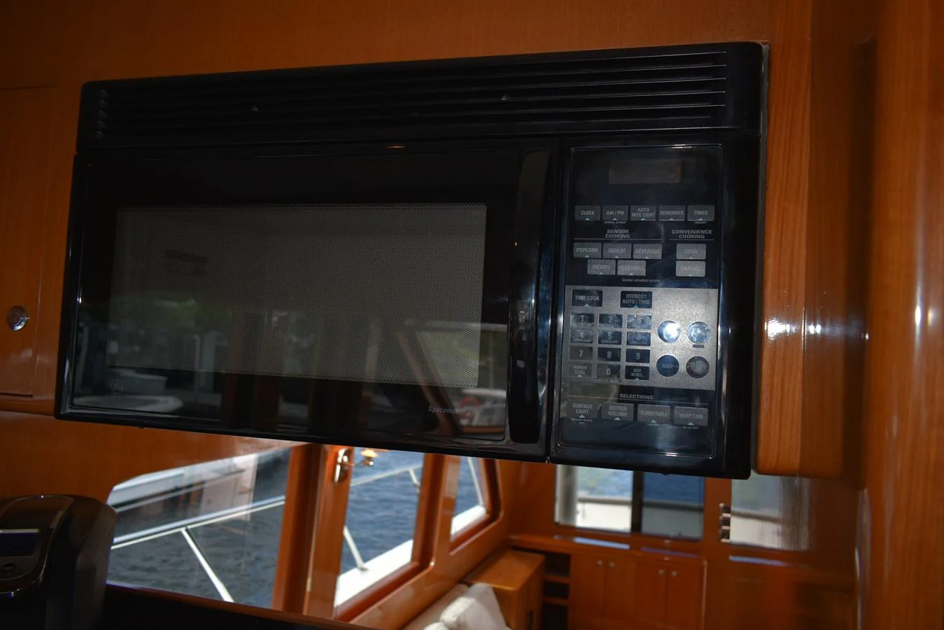 A close-up view of a microwave in the yacht's galley, highlighting the wooden cabinetry and window view. aboard 64 OCEAN ALEXANDER Yacht for Sale