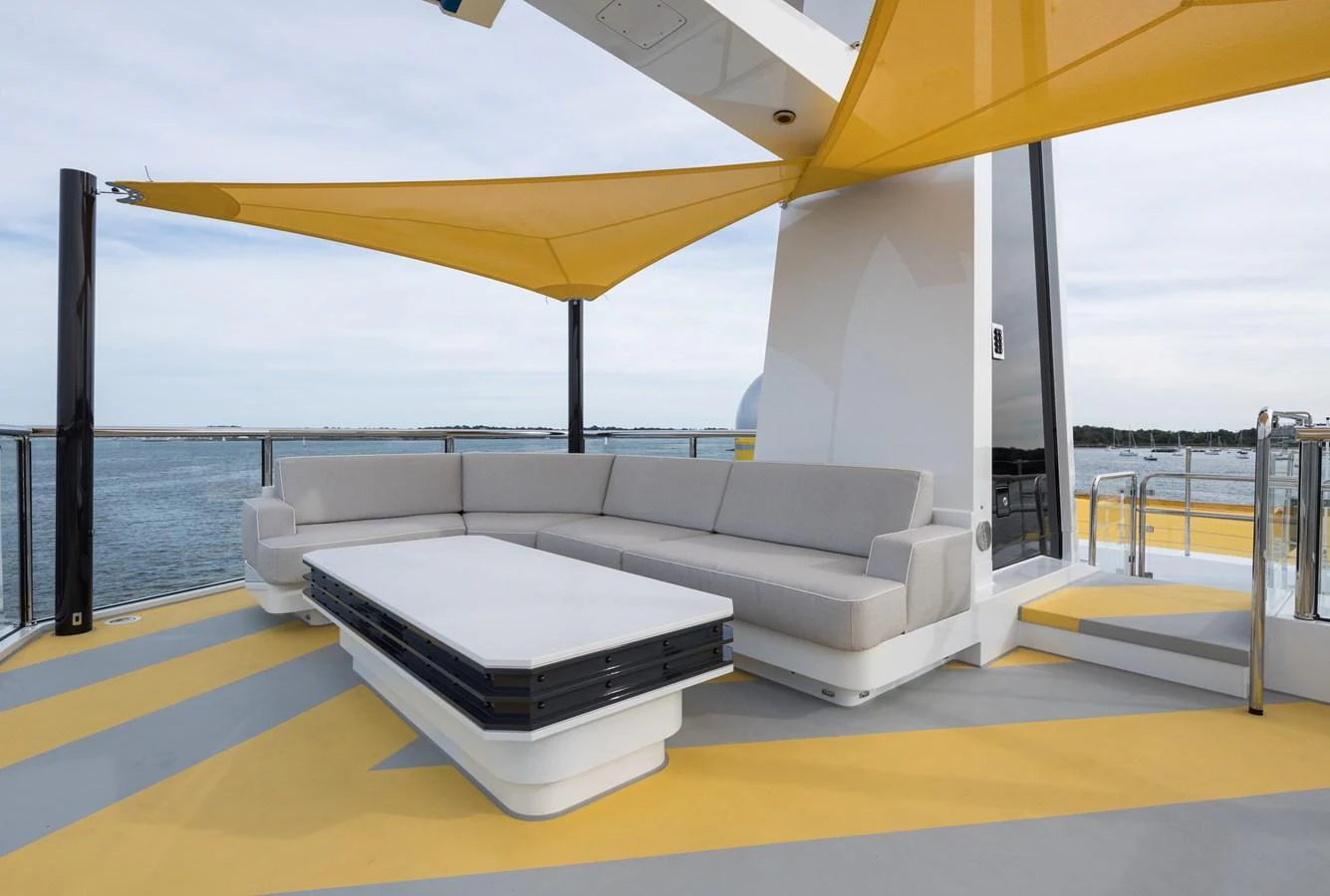 The sundeck features a stylish seating area with a modern sofa and a sleek coffee table under a vibrant yellow canopy. aboard SCOUT Yacht for Sale