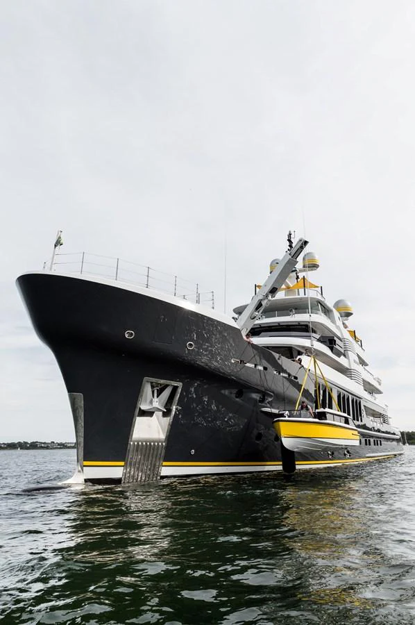 A sleek black yacht with yellow accents is anchored in calm waters. aboard SCOUT Yacht for Sale