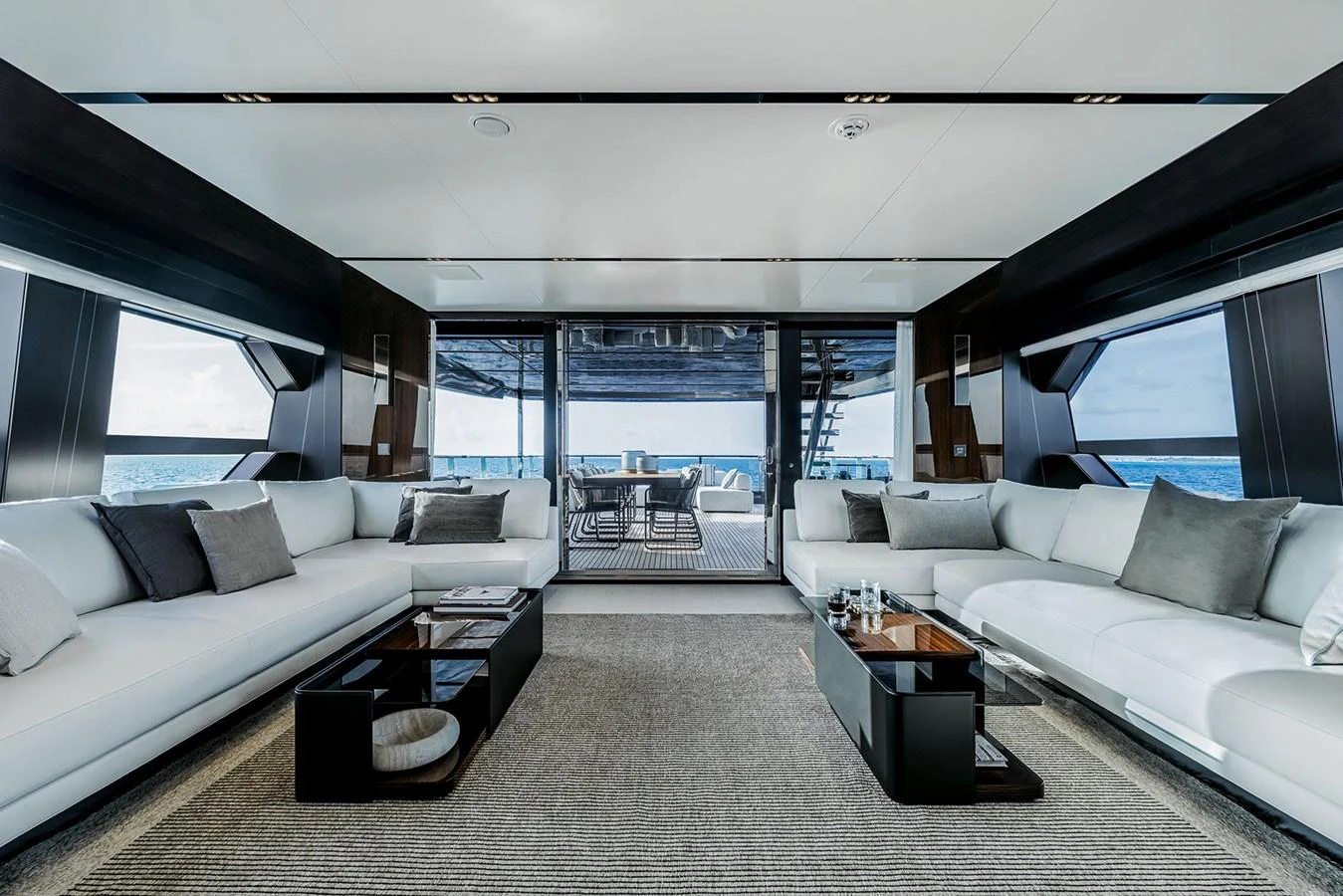 The salon features luxurious seating with a view of the ocean through large windows and an open aft deck. aboard RIVA 130/02 Yacht for Sale
