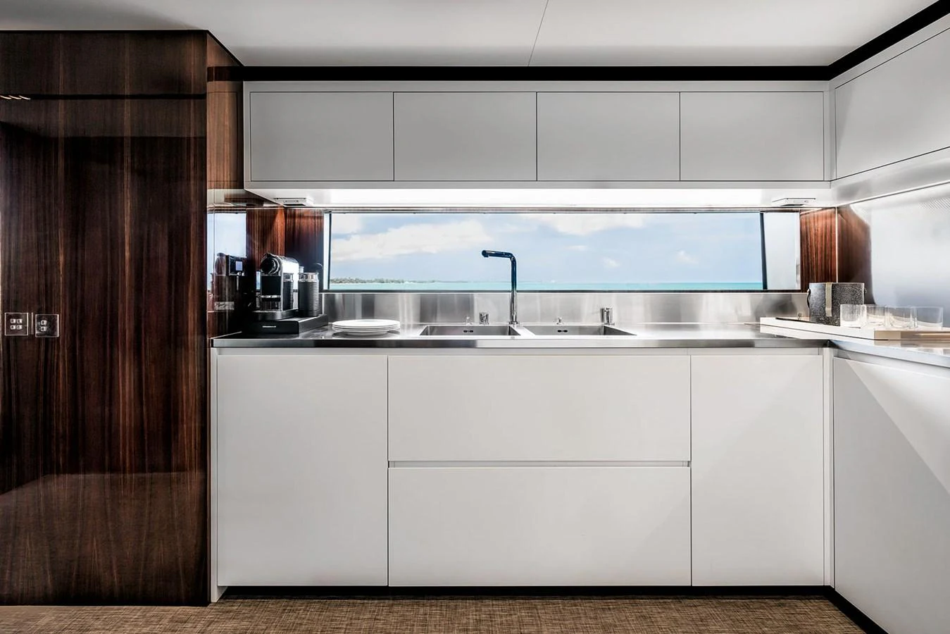 The galley features sleek cabinetry, modern appliances, and a panoramic window with a sea view. aboard RIVA 130/02 Yacht for Sale