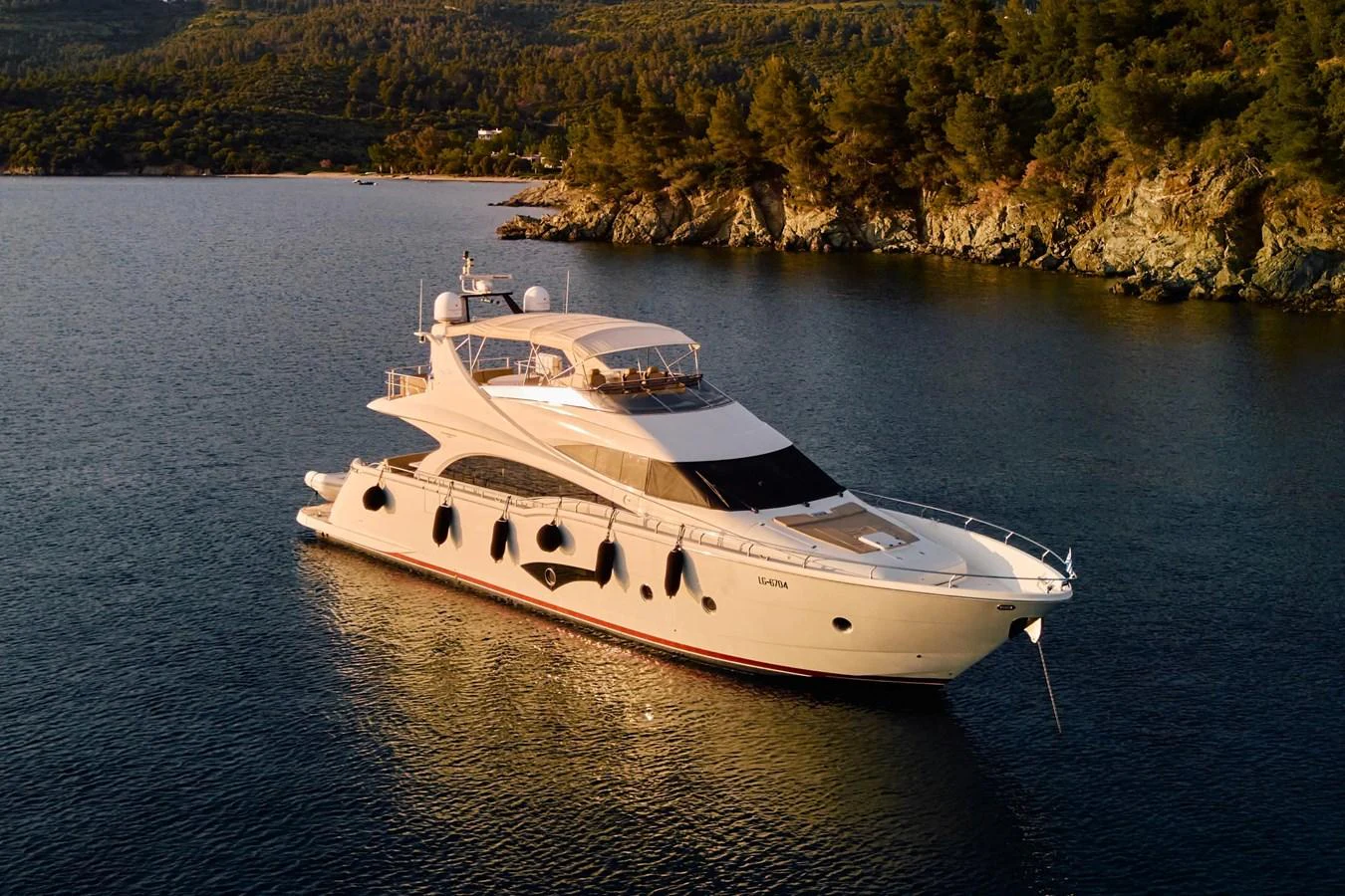 A luxurious yacht is anchored in a serene bay, surrounded by lush greenery and calm waters. aboard MARQUIS 720 Yacht for Sale