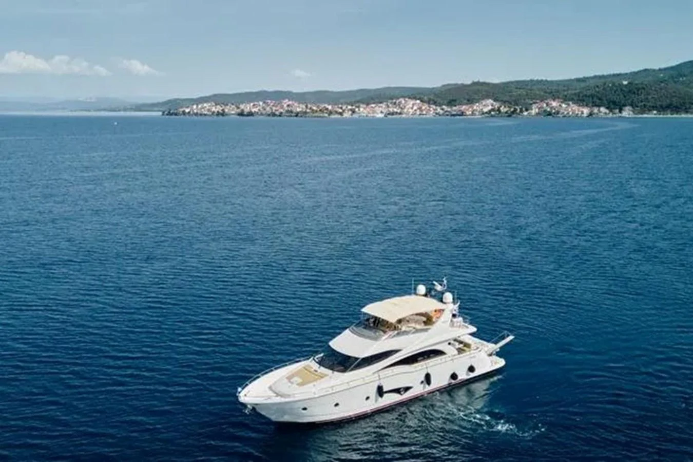 A luxurious yacht cruises through serene blue waters with a picturesque coastline in the background. aboard MARQUIS 720 Yacht for Sale