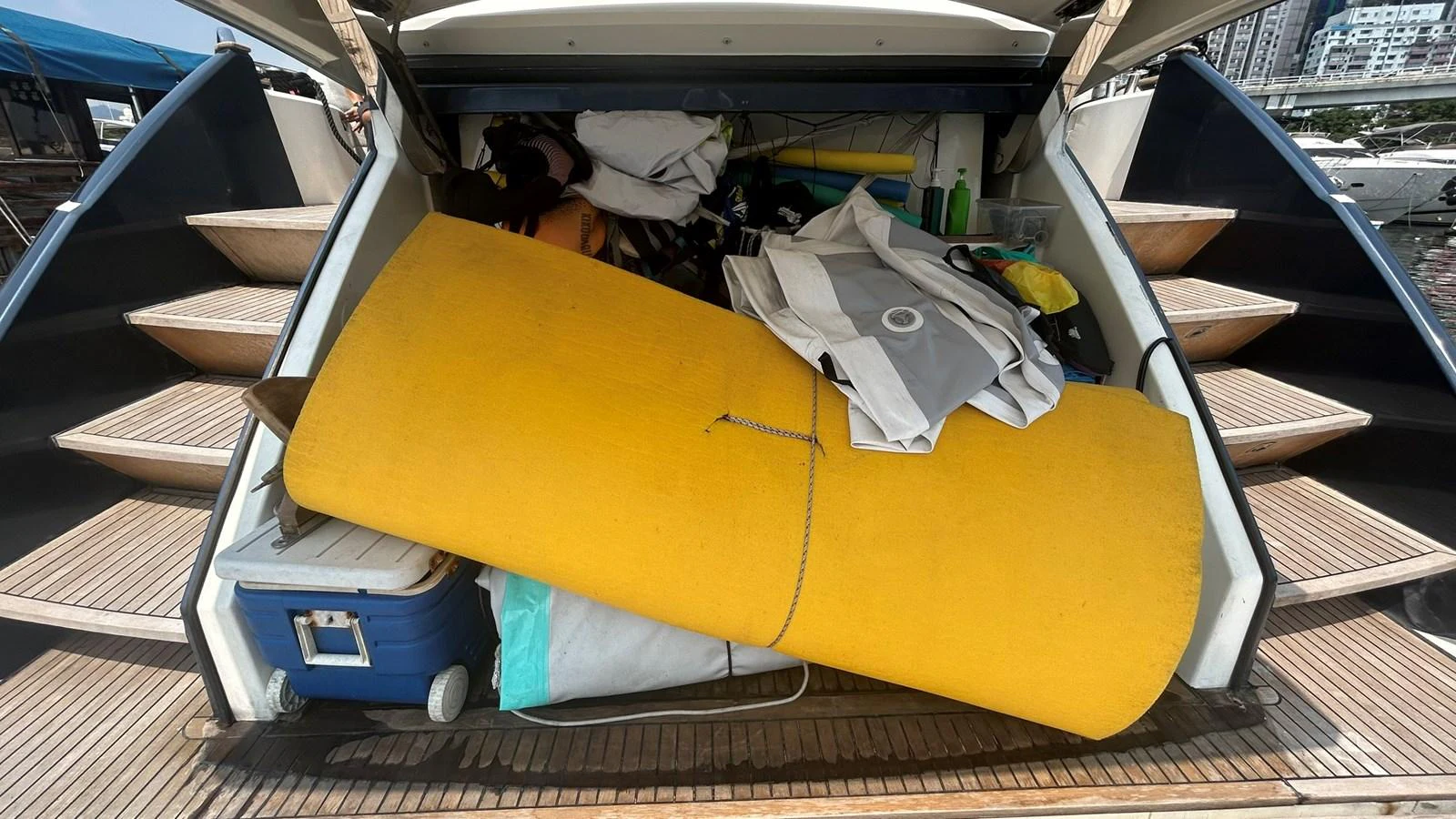 The image shows a cluttered storage area at the stern of the yacht, filled with various items including a yellow mat and a cooler. aboard AURORA Yacht for Sale