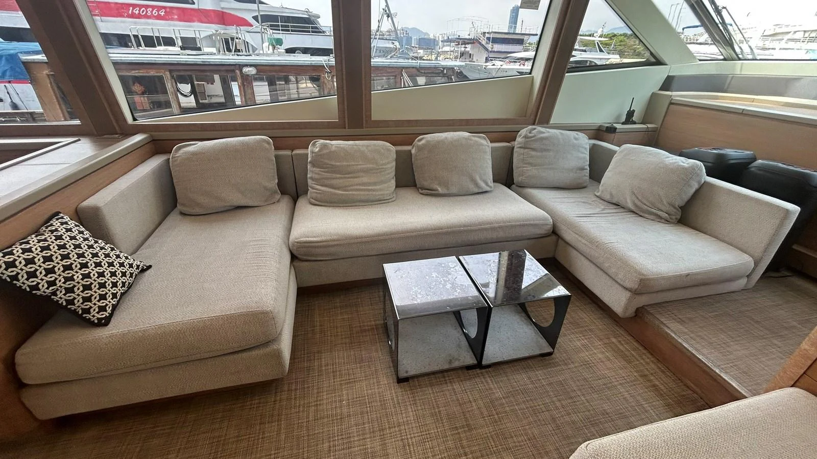 The salon features a comfortable L-shaped sofa with neutral tones and large windows offering marina views. aboard AURORA Yacht for Sale