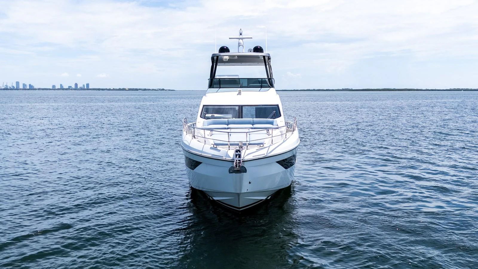 A sleek yacht is pictured head-on, cruising on calm waters with a distant city skyline in the background. aboard GONE PHISHING Yacht for Sale