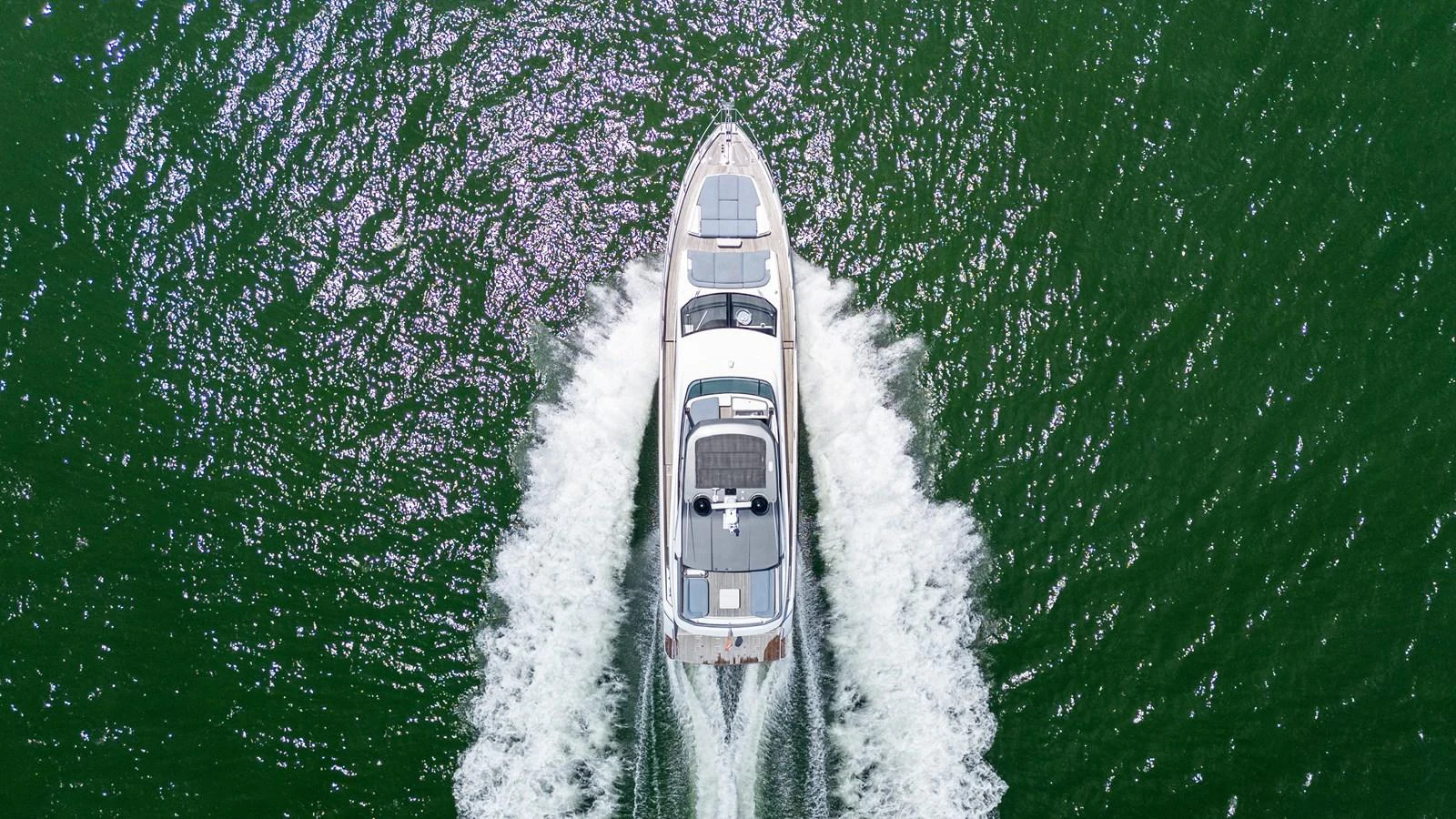 A sleek yacht cruises through vibrant green waters, leaving a trail of white wake behind. aboard GONE PHISHING Yacht for Sale