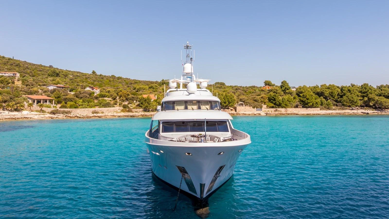 A sleek yacht is anchored in crystal-clear turquoise waters with a scenic coastline in the background. aboard LA STELLA DEI MARI Yacht for Sale