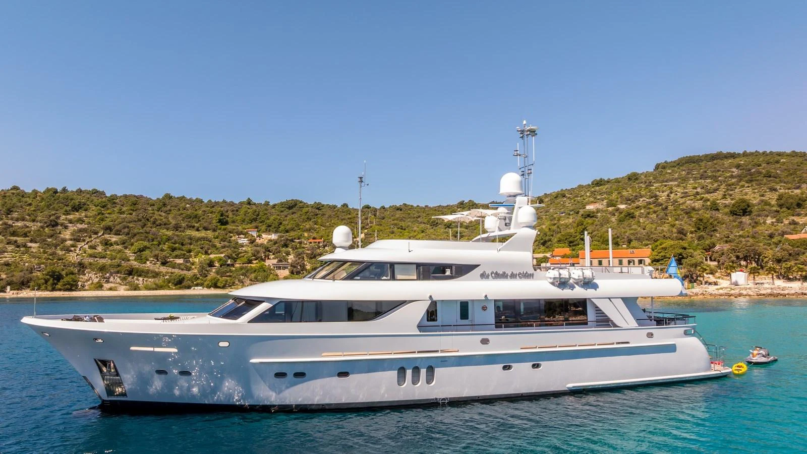 A sleek and elegant yacht is anchored in a serene coastal area with clear blue waters and lush greenery in the background. aboard LA STELLA DEI MARI Yacht for Sale