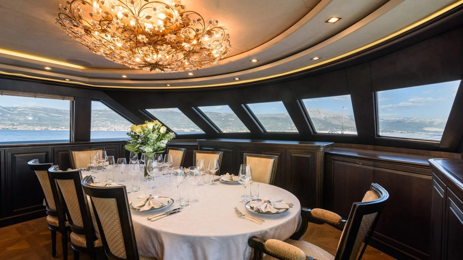 The elegant dining area features a round table set for a formal meal, surrounded by large windows offering panoramic views. aboard LA STELLA DEI MARI Yacht for Sale