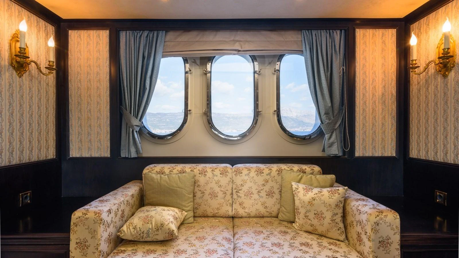 A cozy seating area with a floral-patterned sofa and large porthole windows offering a view of the sea. aboard LA STELLA DEI MARI Yacht for Sale