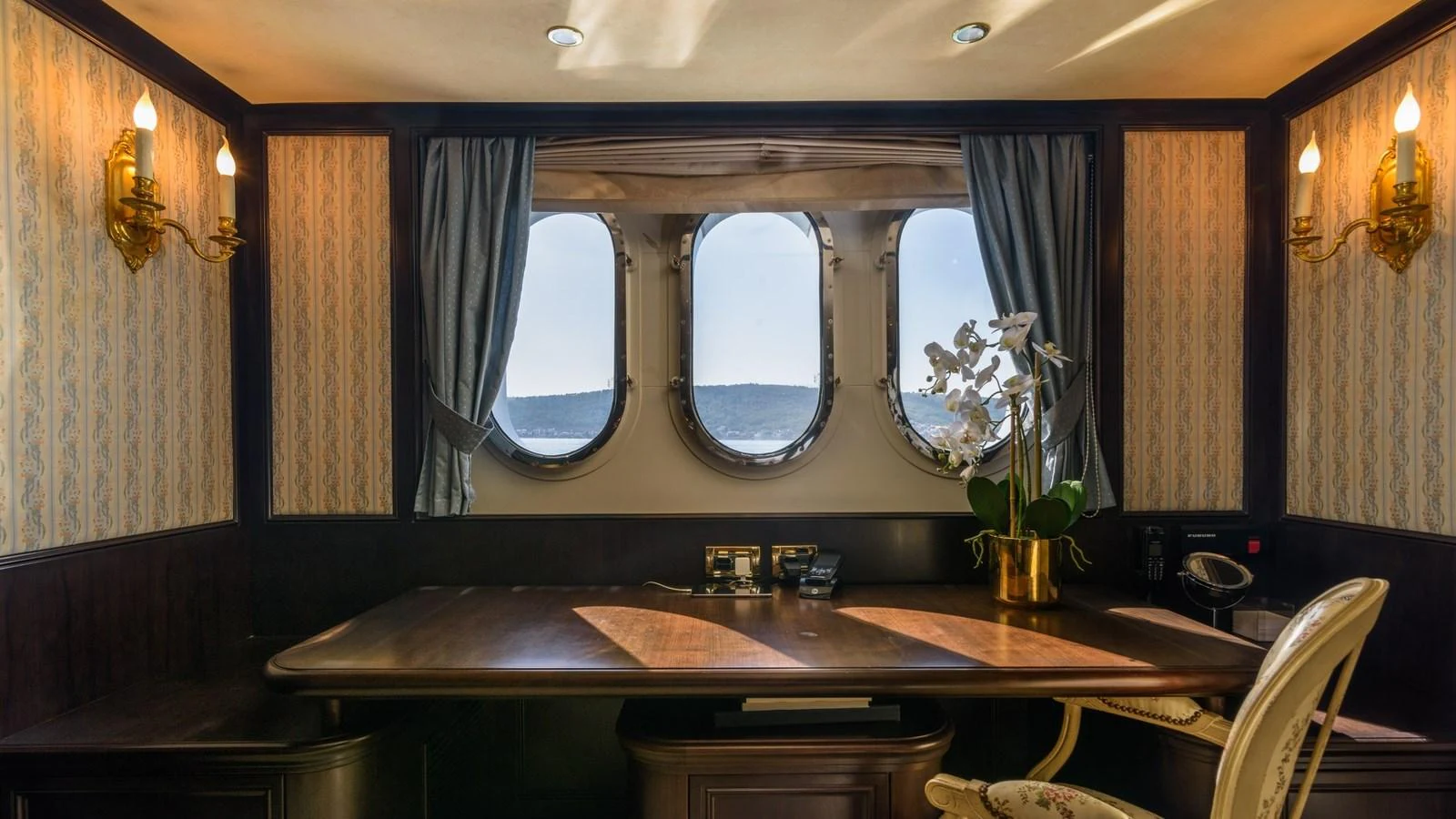 A luxurious yacht office with elegant wood furnishings and a scenic view through porthole windows. aboard LA STELLA DEI MARI Yacht for Sale
