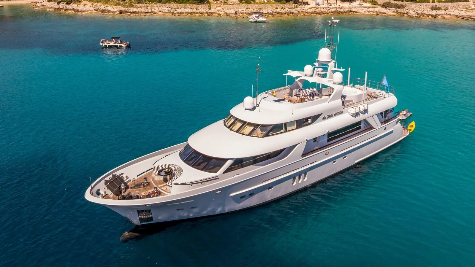 A sleek and elegant yacht cruises through clear turquoise waters near a picturesque coastline. aboard LA STELLA DEI MARI Yacht for Sale