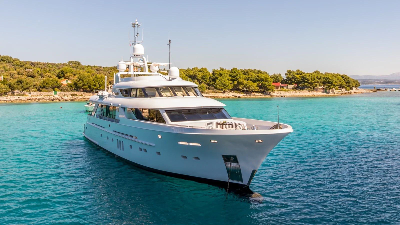 A sleek and elegant yacht is anchored in a serene, turquoise bay with lush greenery in the background. aboard LA STELLA DEI MARI Yacht for Sale