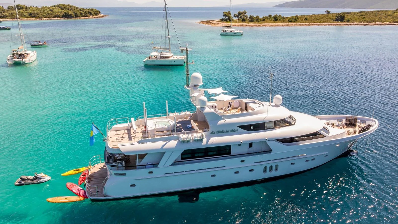 A luxurious yacht is anchored in a serene bay with clear turquoise waters and surrounding sailboats. aboard LA STELLA DEI MARI Yacht for Sale