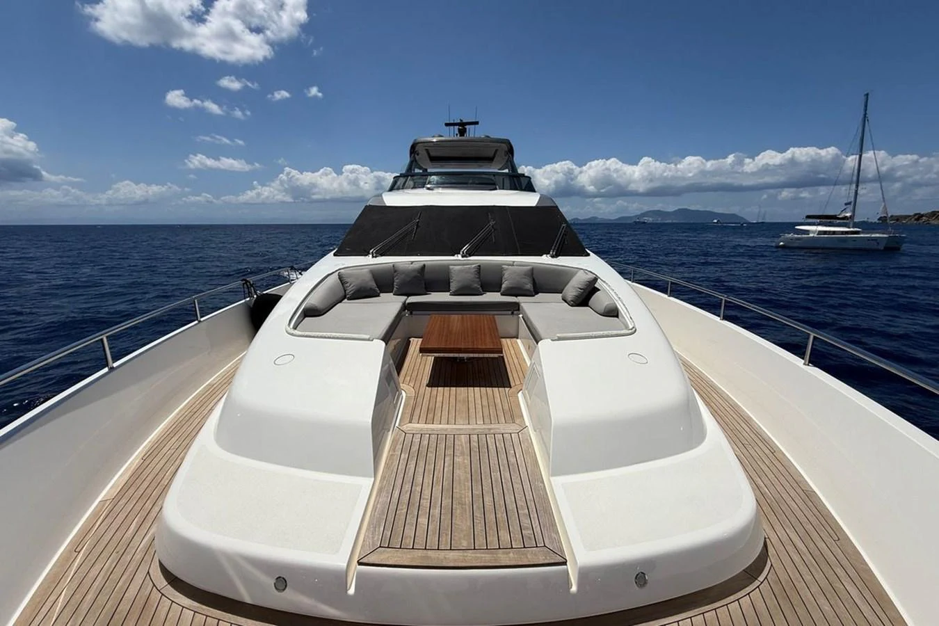 The yacht's foredeck features a spacious sunbathing area with plush seating and a central wooden table, set against a stunning ocean backdrop. aboard CUT Yacht for Sale