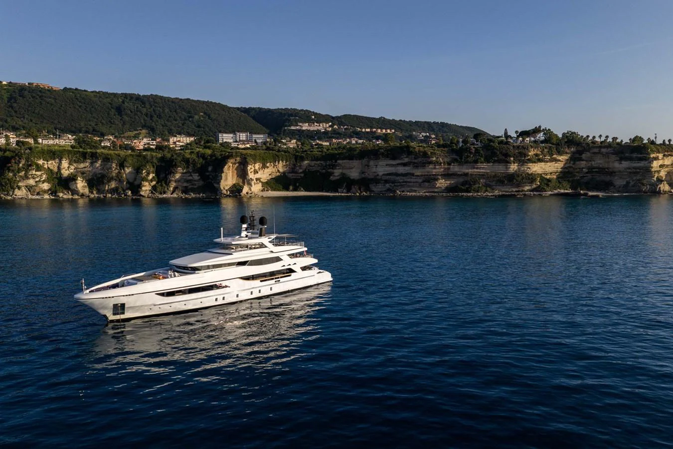 A sleek, modern yacht cruises along a tranquil coastline under a clear sky. aboard MR. T Yacht for Sale