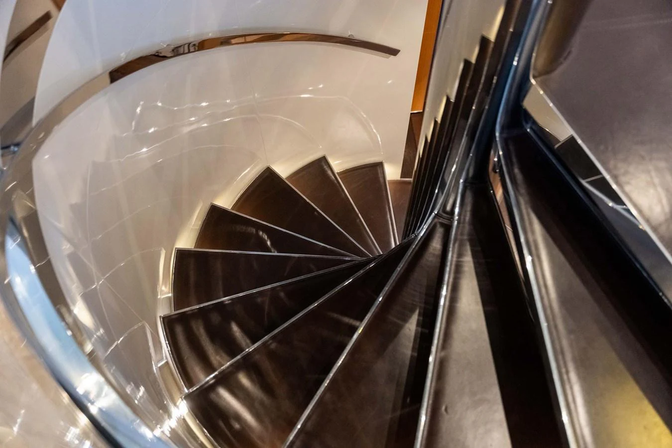 A sleek, modern spiral staircase with polished metal railings and dark wooden steps. aboard MR. T Yacht for Sale