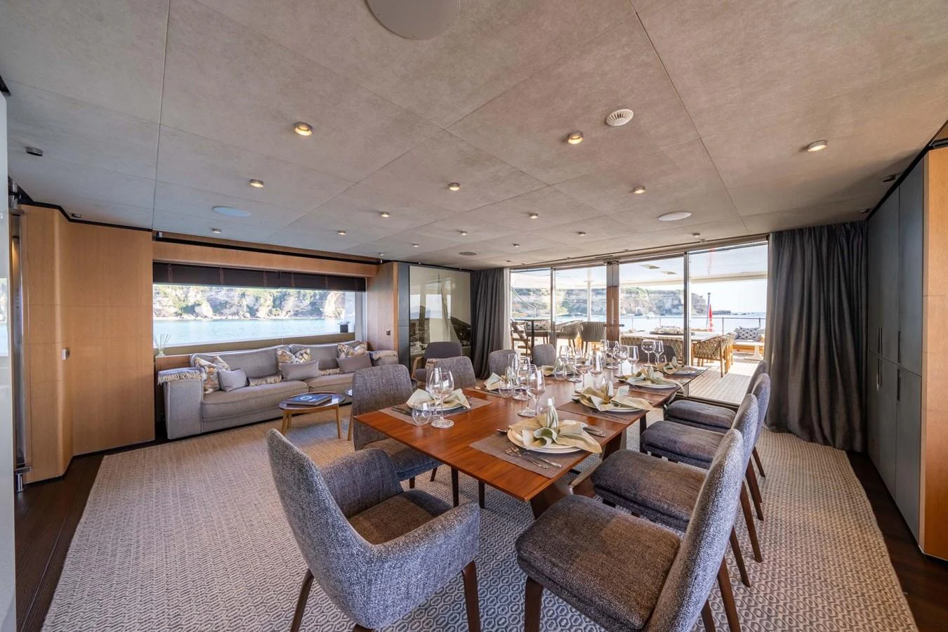 The yacht's dining area features a spacious table set for a formal meal, complemented by a comfortable lounge area and large windows offering scenic views. aboard MR. T Yacht for Sale