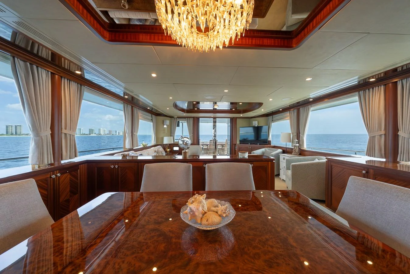 The yacht's salon features elegant wood finishes, a stunning chandelier, and expansive windows offering panoramic ocean views. aboard ABOAT TIME Yacht for Sale
