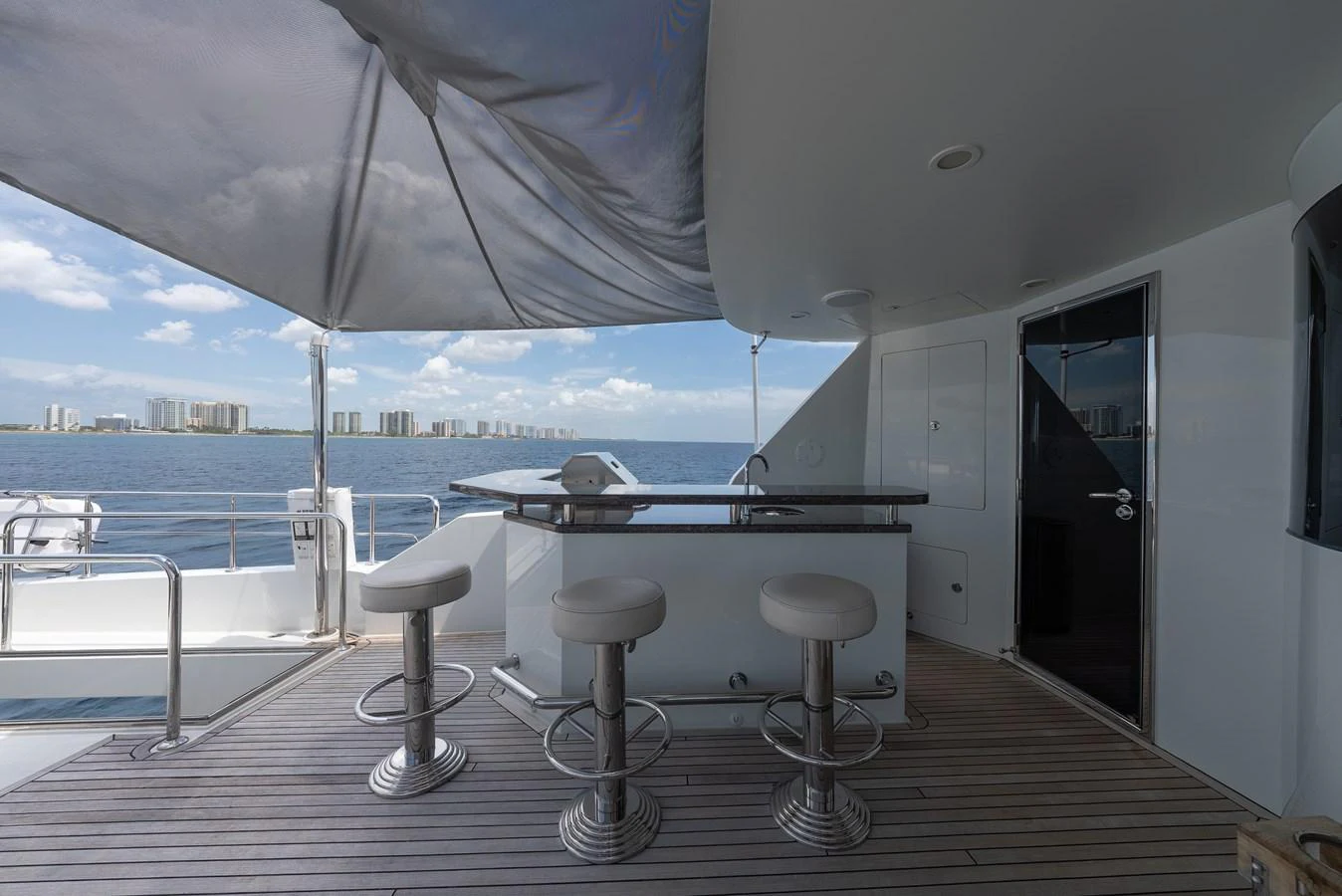 The aft deck features a sleek bar area with modern stools and a shaded canopy, offering a perfect spot for relaxation and socializing. aboard ABOAT TIME Yacht for Sale