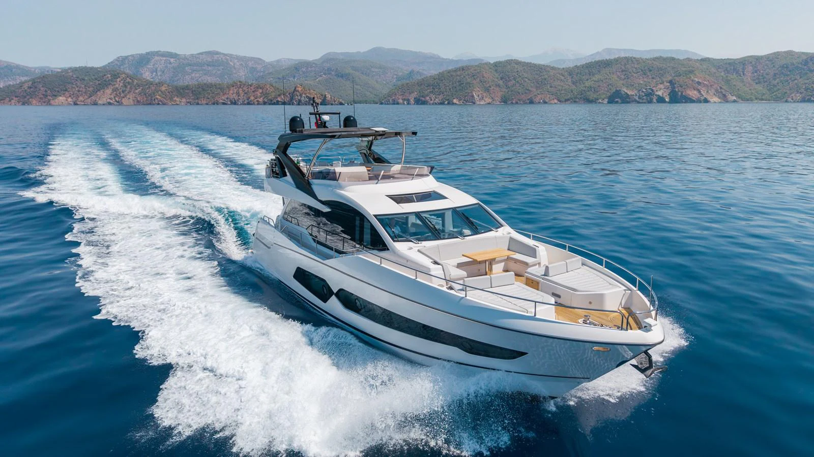 A sleek and modern yacht cruises through clear blue waters with scenic mountains in the background. aboard NAAMA Yacht for Sale