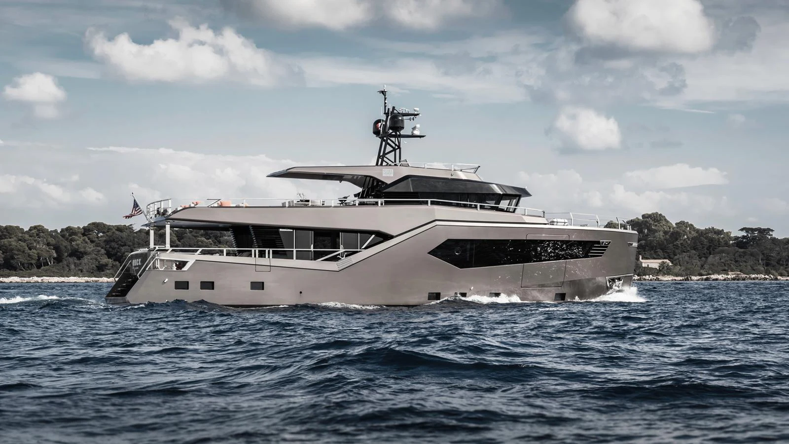 A sleek and modern yacht cruises through the water under a partly cloudy sky. aboard HULL #5 Yacht for Sale