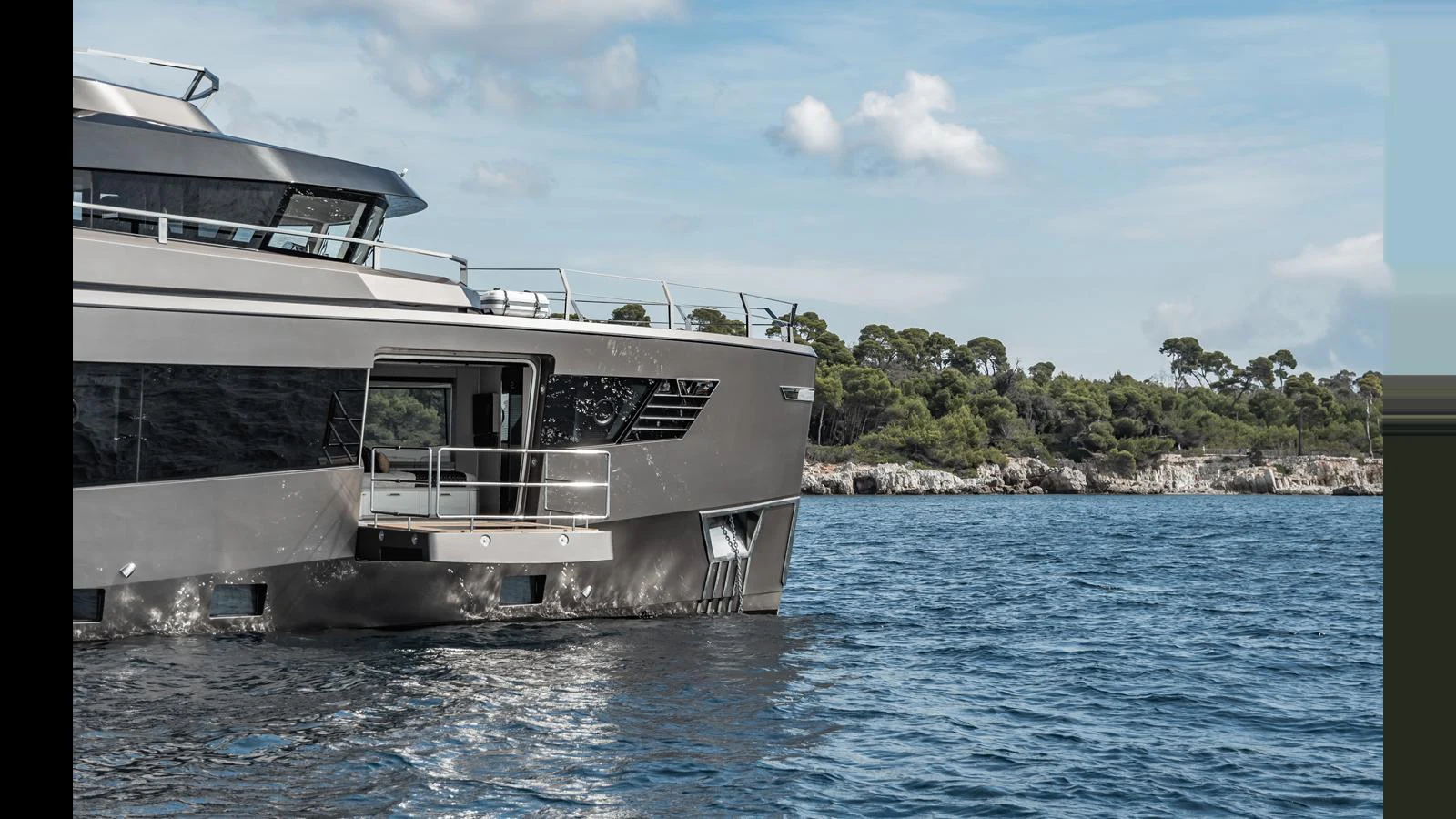 A sleek yacht cruising near a scenic coastline under a partly cloudy sky. aboard HULL #5 Yacht for Sale