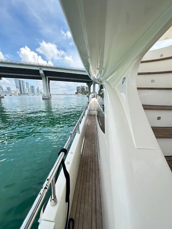 A sleek side deck of a yacht with a view of the city skyline and a bridge in the background. aboard 75FT AZIMUT 2010, MINIMAL RISK Yacht for Sale