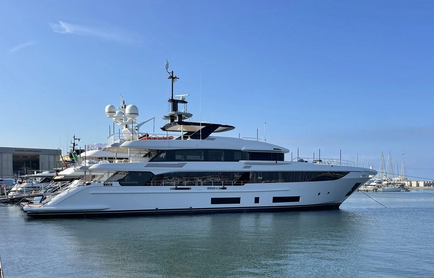 A sleek and modern yacht is docked in a serene marina under a clear blue sky. aboard LUMINA Yacht for Sale