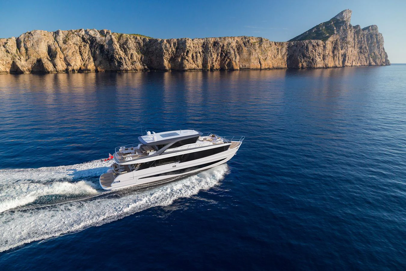 A sleek yacht cruises along a stunning coastal landscape with clear blue waters and rocky cliffs in the background. aboard PRINCESS X90 Yacht for Sale