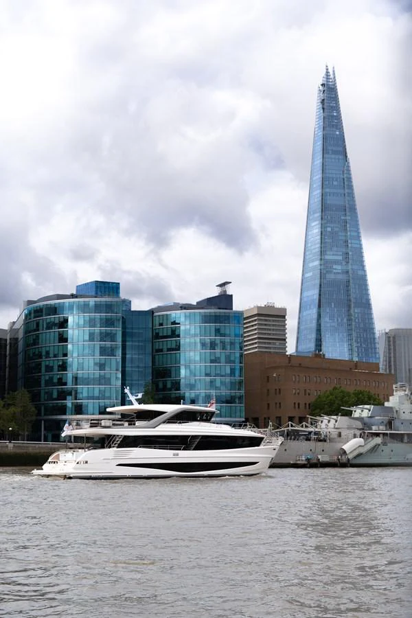 A sleek yacht cruises along a city waterfront with modern buildings in the background. aboard PRINCESS X90 Yacht for Sale