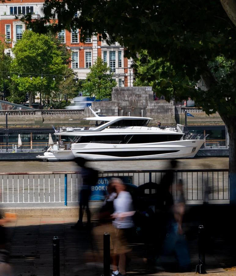 A sleek yacht is docked along a picturesque waterfront, framed by urban architecture and lush greenery. aboard PRINCESS X90 Yacht for Sale