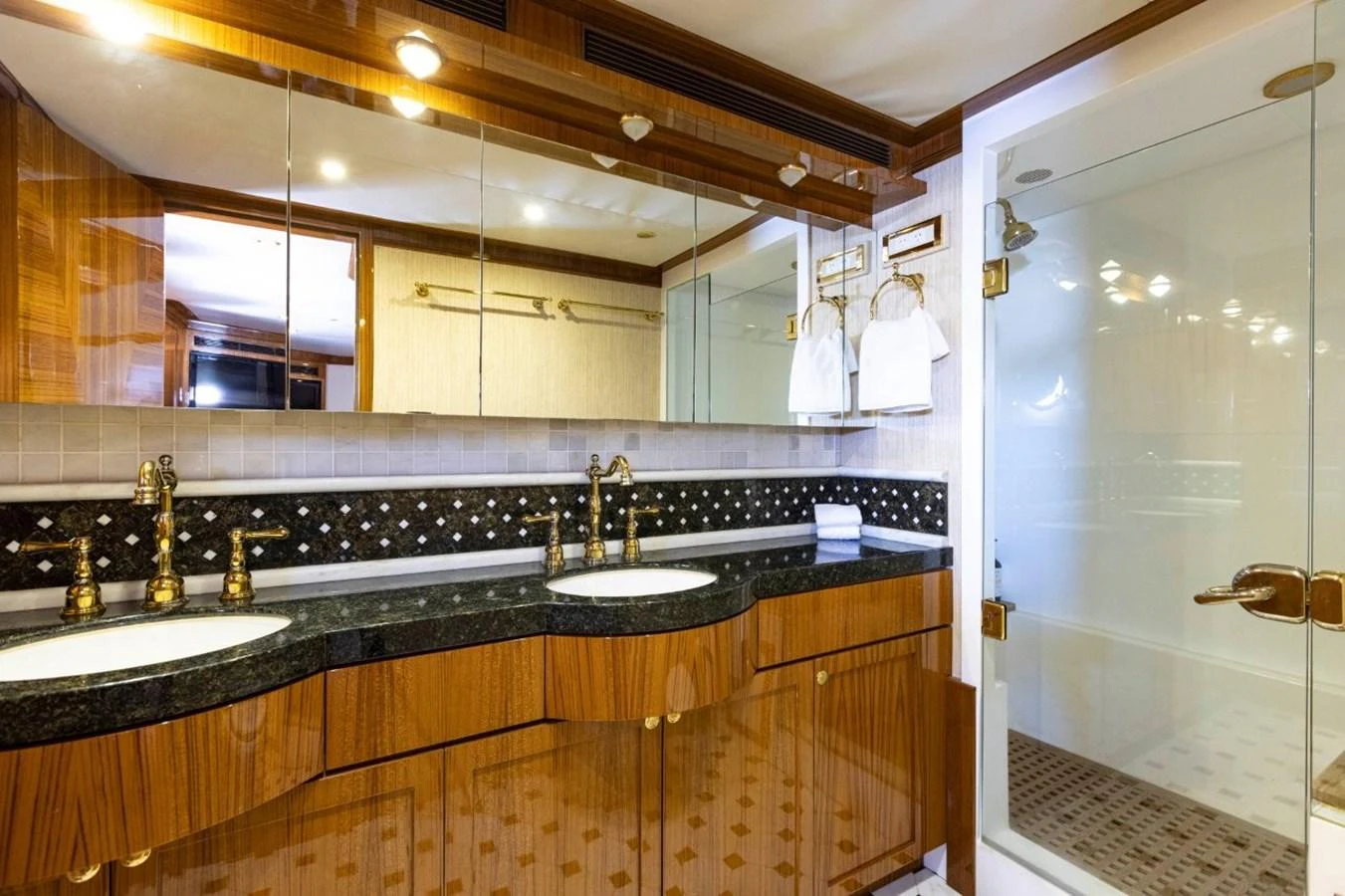 The yacht's bathroom features elegant wood finishes, dual sinks, and a spacious glass-enclosed shower. aboard ODYSSEY Yacht for Sale