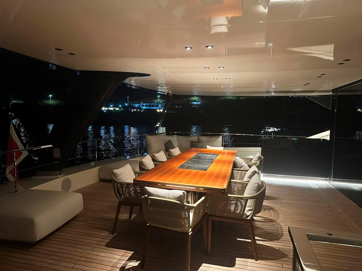 The aft deck features a stylish dining area with a sleek wooden table and comfortable seating, perfect for evening gatherings. aboard ATALI Yacht for Sale