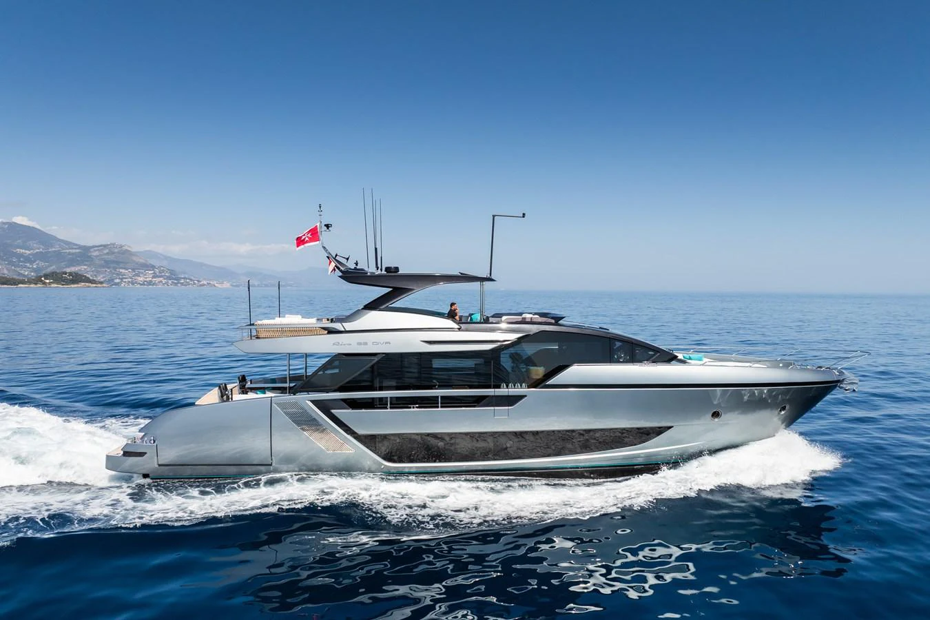 A sleek and modern yacht glides through the calm blue waters under a clear sky. aboard L'AS BLEU Yacht for Sale