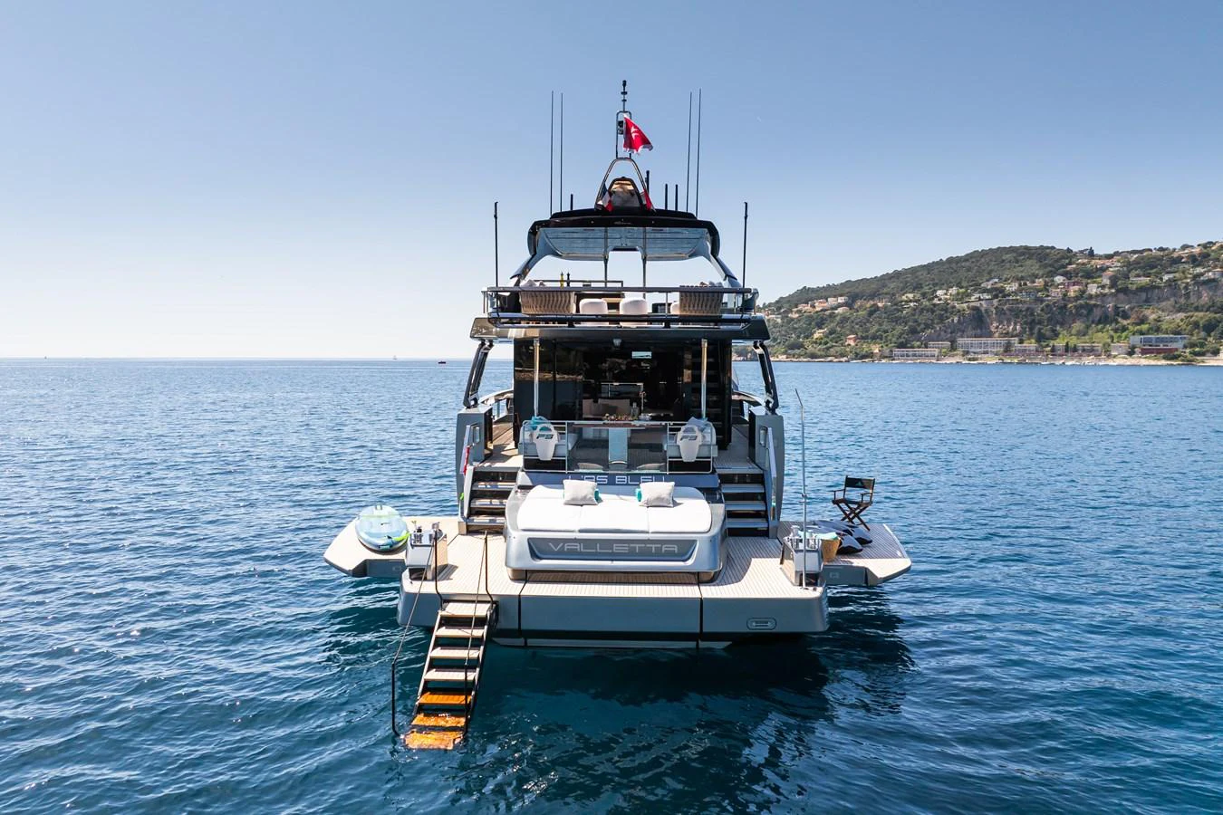 A luxurious yacht anchored in serene blue waters with a view of the coastline. aboard L'AS BLEU Yacht for Sale