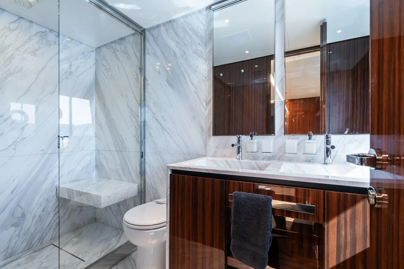 The bathroom features elegant marble walls and a sleek wooden vanity with dual sinks. aboard L'AS BLEU Yacht for Sale