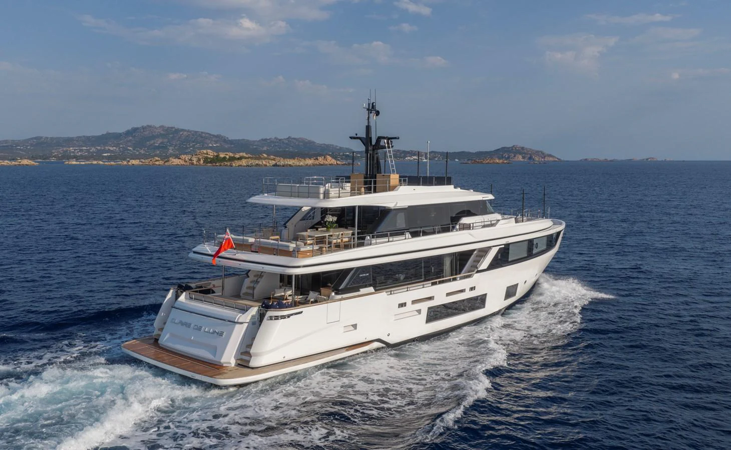 A sleek and modern yacht cruises through open waters with a scenic backdrop of distant islands. aboard CLAIRE DE LUNE Yacht for Sale